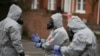 U.K. -- Military personnel wearing protective coveralls work to remove vehicles from a cordoned off area behind a police station in Salisbury, March 11, 2018